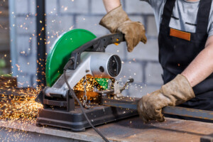 industrial worker cutting metal with mitre saw